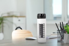 Die WEPA 2in1 Trinkflasche mit 1x7 Medikamentendosierer in weiß auf einem Schreibtisch.