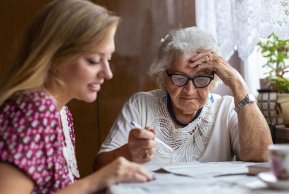Eine jüngere und eine ältere Dame, die gemeinsam an einem Tisch sitzen und einen Brief lesen.
